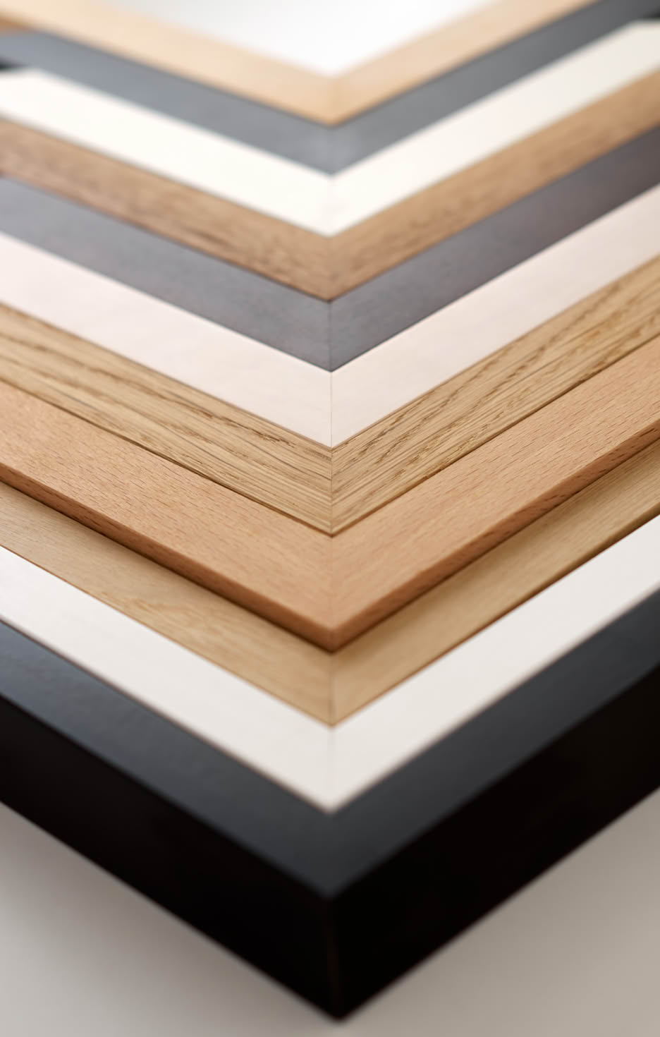 Mehrere hintereinander gelegte Holz-Bilderrahmen-Winkel in verschiedenen Farben und Holzarten.